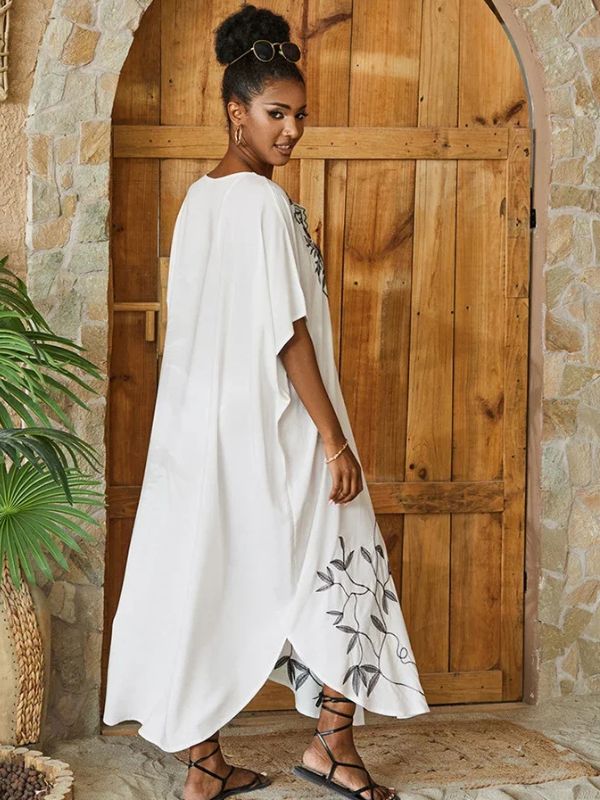 Vue arrière d&#39;une femme en djellaba blanche ample avec motifs végétaux noirs près d&#39;une porte en pierre