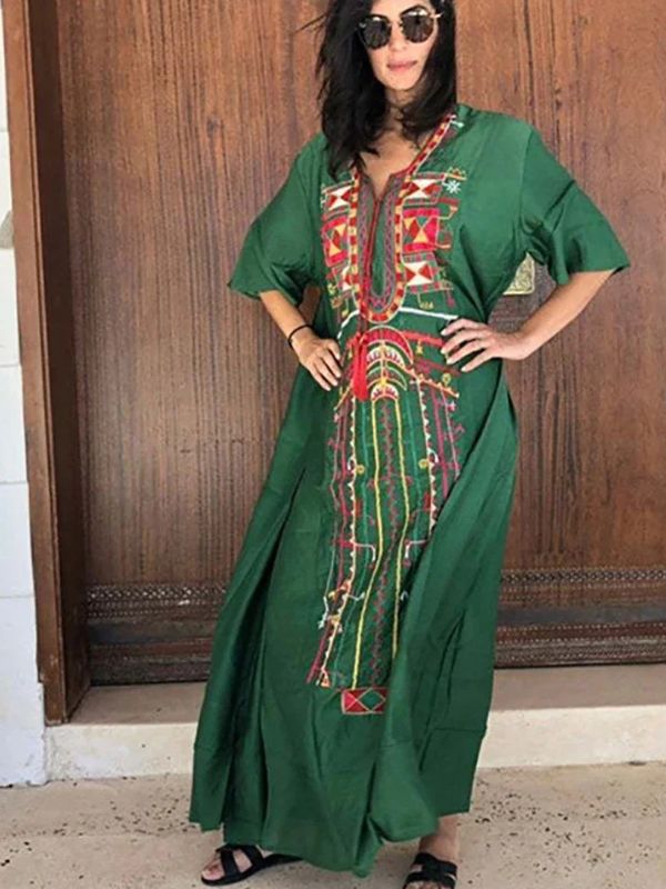 Une femme porte une djellaba marocaine verte ornée de broderies amazighes rouges et jaunes, posant devant une porte en bois