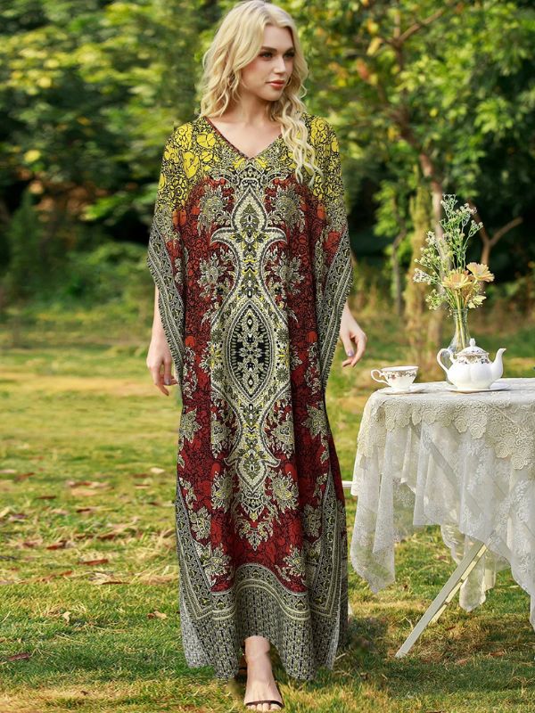 Femme portant une djellaba marocaine rouge et dorée à motifs orientaux, debout dans un jardin près d’une table de thé