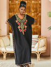 Femme en djellaba noire brodée de fleurs rouges et détails dorés, posant devant une porte en bois sculpté