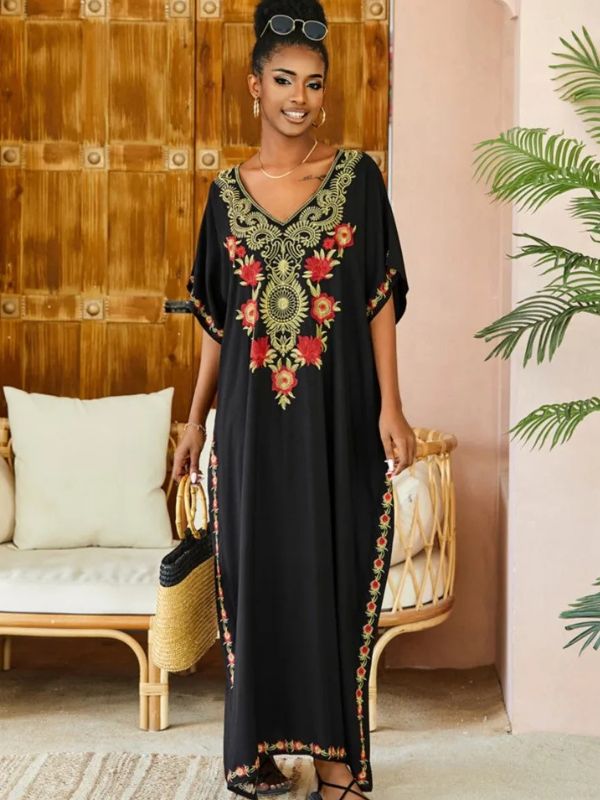 Femme souriante en djellaba noire avec décorations florales, tenant un sac en osier dans un intérieur cosy