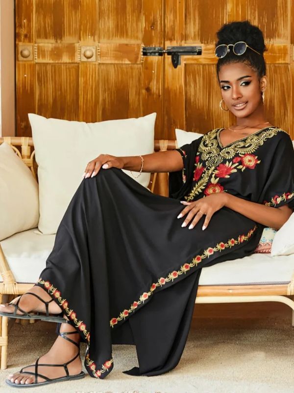 Femme assise en djellaba noire à broderies rouges et dorées, élégamment installée sur un canapé en rotin