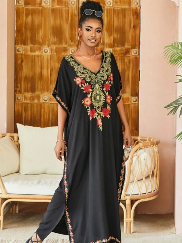 Femme debout en djellaba noire décorée de broderies dorées et rouges, posant devant un décor intérieur en rotin