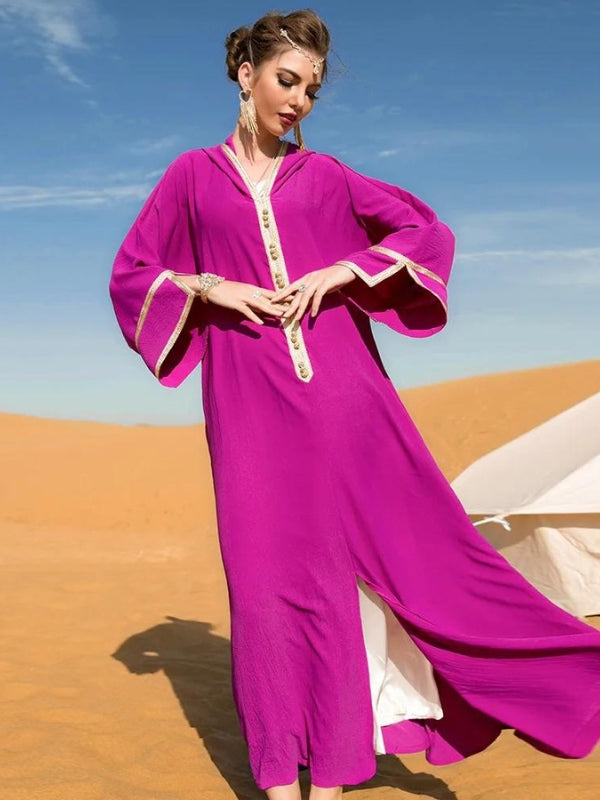 Femme debout dans le désert portant une djellaba marocaine fuchsia fluide avec des finitions dorées, posant sous un ciel bleu clair