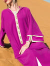 Femme assise dans le sable portant une djellaba marocaine fuchsia ornée de détails dorés, mettant en valeur des accessoires élégants