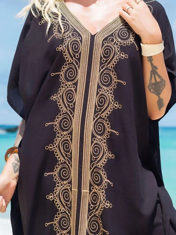 Gros plan sur une djellaba noire décorée de motifs dorés raffinés, portée par une femme sur le sable