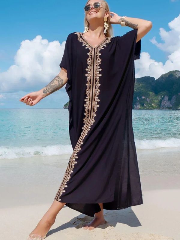 Femme souriante en djellaba noire ornée de broderies dorées, posant sur une plage tropicale