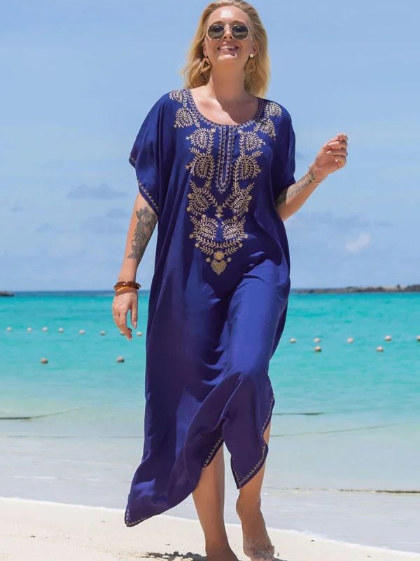 Femme marchant pieds nus sur le sable en djellaba bleu roi avec motifs dorés, en bord de mer turquoise