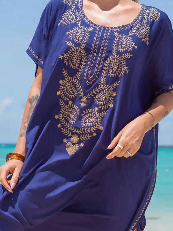 Gros plan sur une djellaba bleu roi ornée de broderies dorées, portée par une femme sur une plage tropicale