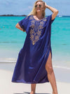 Femme en djellaba bleu roi fendue sur le côté, souriant et posant sur le sable face à la mer