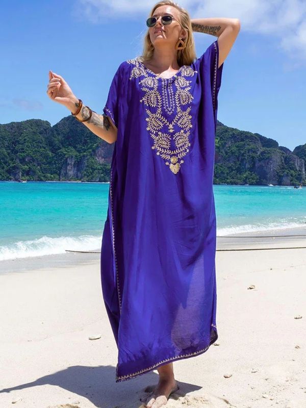 Femme portant une djellaba bleu roi à motifs dorés, posant sur une plage avec vue sur des montagnes verdoyantes
