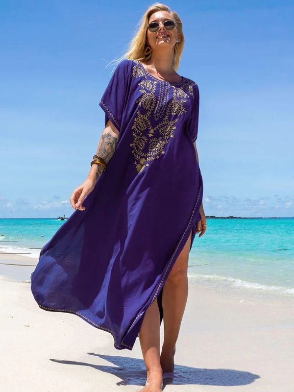 Femme en djellaba bleu roi avec broderies dorées, posant face à la mer sous un ciel ensoleillé