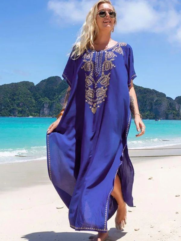 Femme souriante en djellaba bleu roi ornée de broderies dorées, marchant sur une plage tropicale
