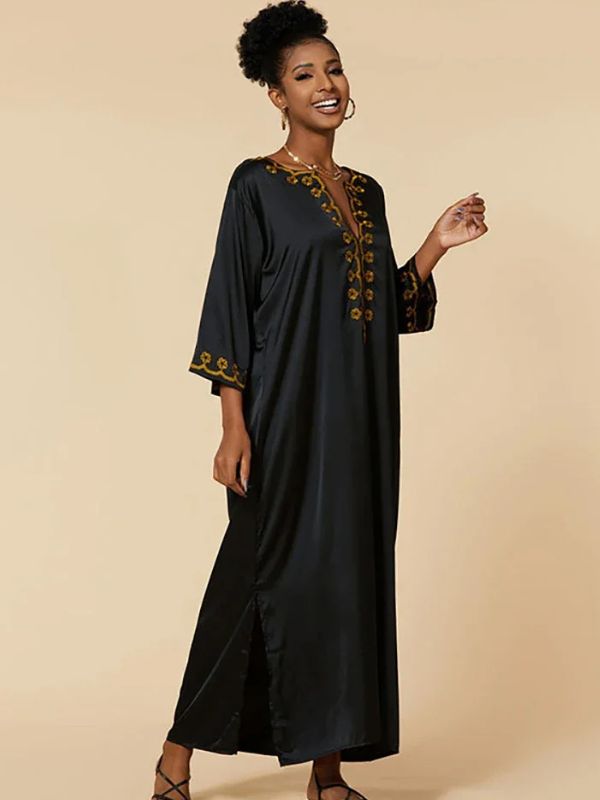 Femme souriante en djellaba noire élégante, levant la main avec légèreté.