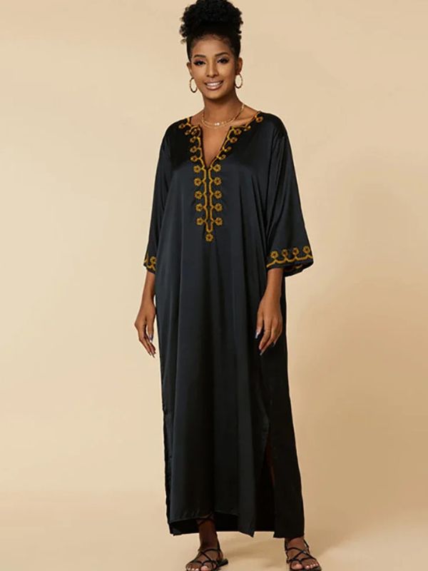 Portrait de face d’une femme souriante en djellaba noire, broderies dorées au col et aux manches