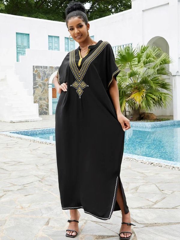 Femme en djellaba marocaine noire brodée tenant les pans de sa robe, posant près d’une piscine