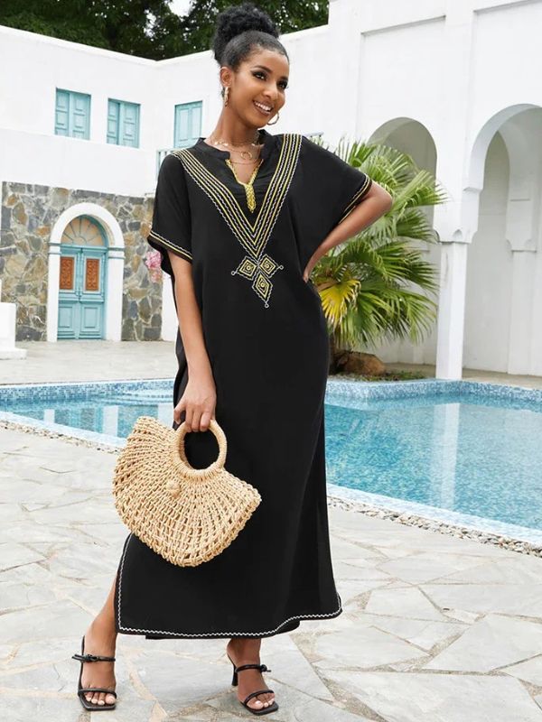 Femme en djellaba marocaine noire brodée posant près d’une piscine, tenant un sac en paille rond