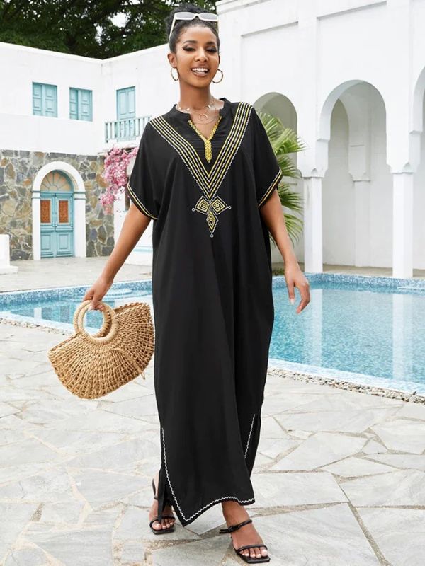 Femme portant une djellaba marocaine noire brodée, marchant près d’une piscine, avec un sac en paille rond