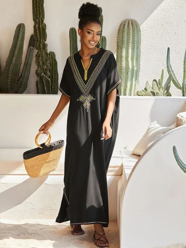 Femme souriante en djellaba marocaine noire brodée, tenant un sac en paille, assise près de cactus