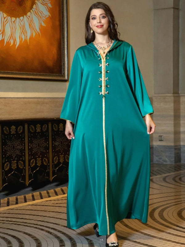 Une femme porte une djellaba vert émeraude avec des bordures dorées, posant avec élégance dans un cadre intérieur chic