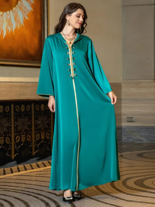 Une femme porte une djellaba vert émeraude avec des bordures dorées, posant avec élégance dans un cadre intérieur chic