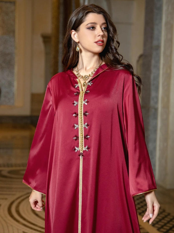 Une femme regarde sur le côté en portant une djellaba grenat ornée de détails dorés et de motifs floraux