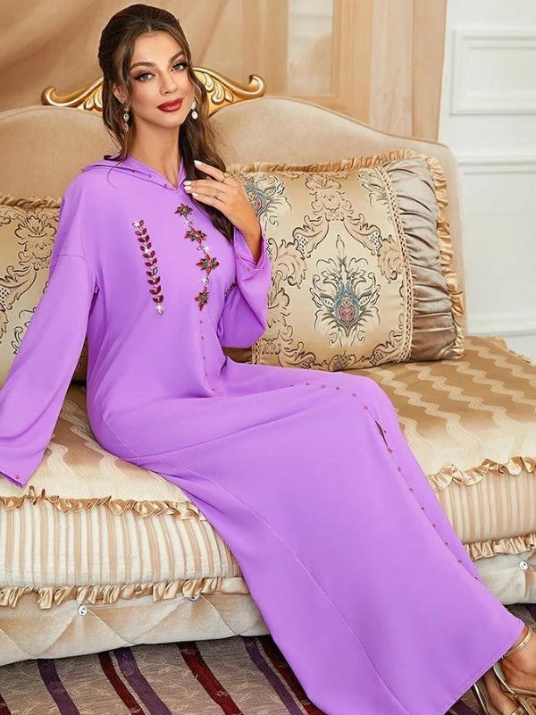 Une djellaba longue de couleur lavande avec des détails élégants, ornée de broderies sur le devant, apporte une touche de sophistication et de modernité. Le design fluide et le tissu léger créent une silhouette gracieuse, tandis que les manches longues offrent une couverture élégante. Le modèle se tient dans un cadre luxueux, accentuant l’élégance du vêtement. Les boucles d'oreilles pendantes ajoutent un éclat supplémentaire, tandis que le style général reste sobre et chic, parfait pour des occasions