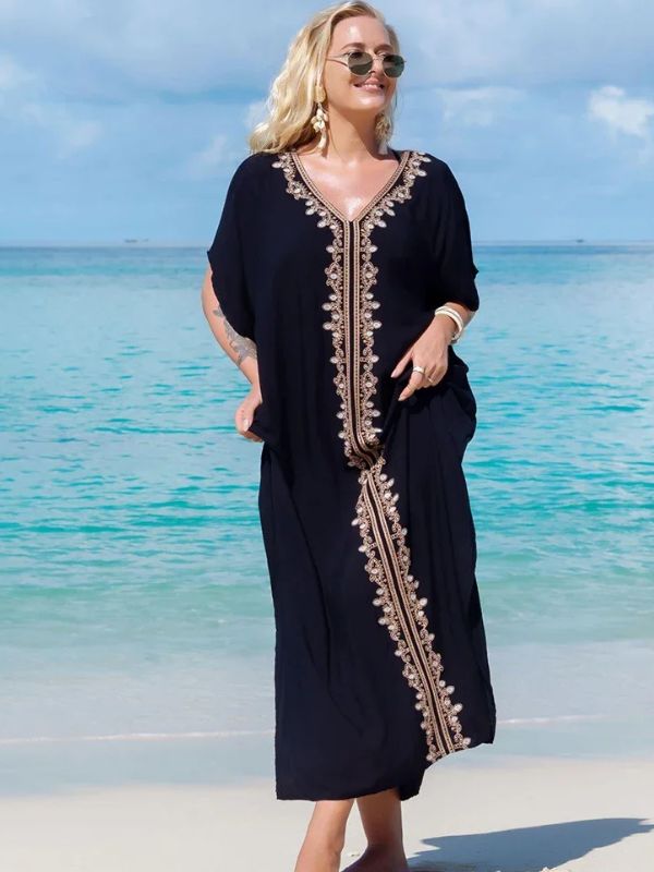 Femme marchant sur une plage en djellaba noire ornée de broderies dorées raffinées