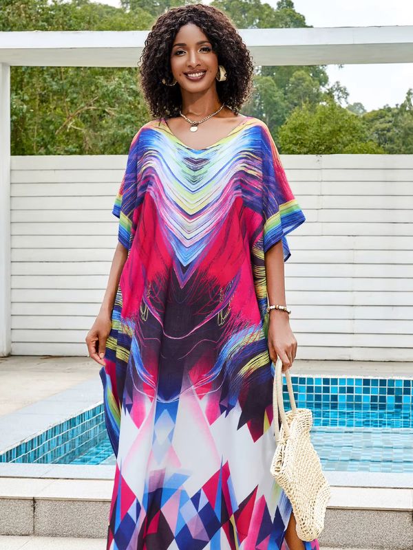 Une femme porte une djellaba longue aux motifs géométriques multicolores, posant près d’une piscine avec un sac tressé à la main