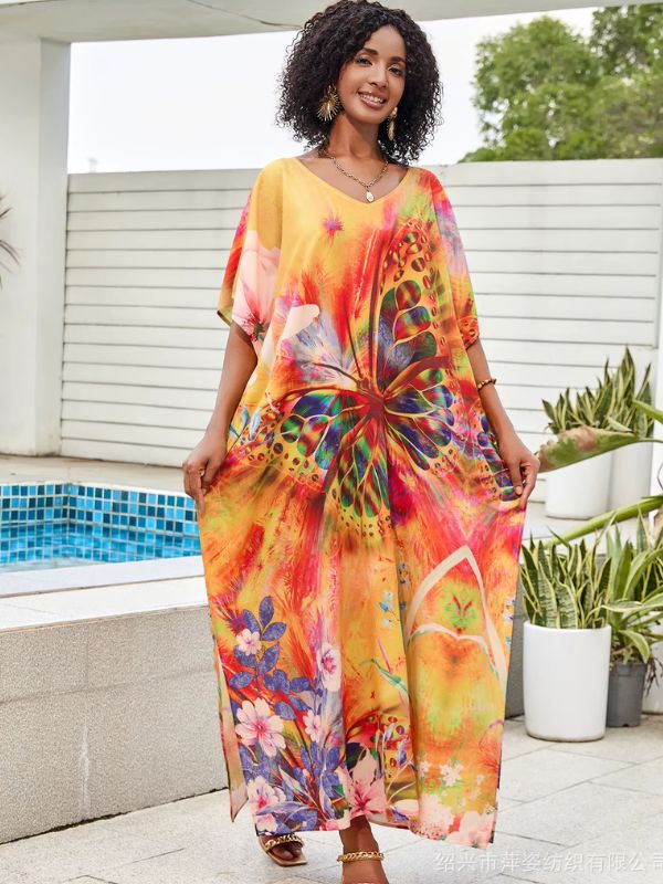 Une femme porte une djellaba jaune et orange ornée d’un grand papillon coloré et de motifs floraux, posant près d’une piscine