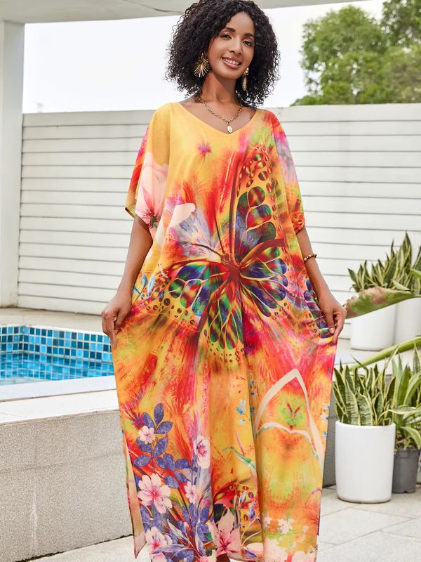 Une femme porte une djellaba jaune et orange ornée d’un grand papillon coloré et de motifs floraux, posant près d’une piscine