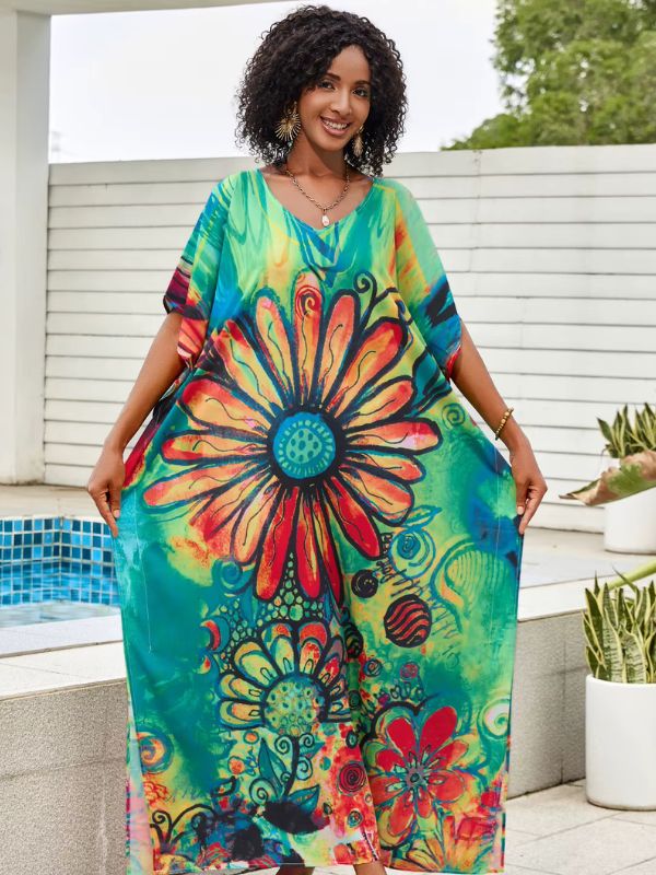 Une femme porte une djellaba colorée ornée d’un grand motif floral rouge et orange sur fond vert et bleu, posant près d’une piscine