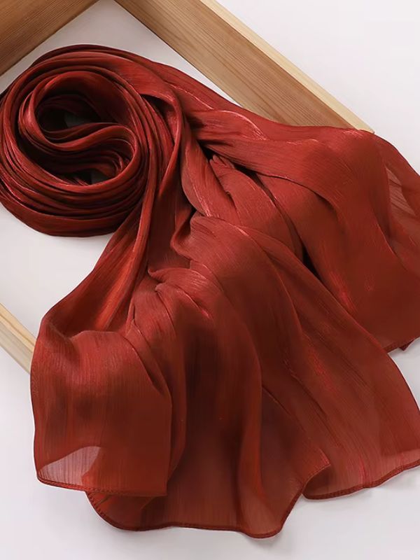 Hijab en mousseline de soie froissée marsala aux reflets shimmer satinés, présenté enroulé sur un plateau en bois naturel