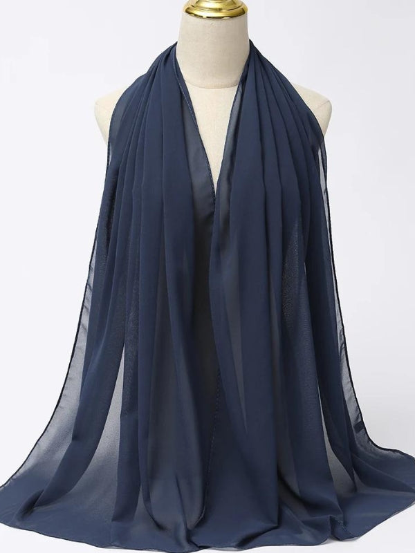 Ce hijab de couleur bleu marine est drapé sur un mannequin, mettant en valeur sa texture fluide et légère. La teinte sombre du bleu marine apporte une touche d'élégance et de sophistication, parfaite pour une tenue formelle ou pour une occasion spéciale. Le tissu semble doux et confortable, offrant à la fois une couverture complète et une sensation de légèreté