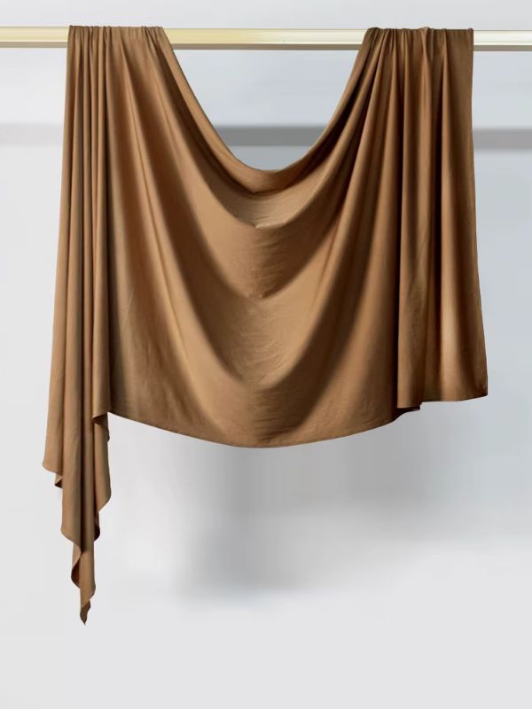 Hijab en jersey camel suspendu et drapé sur une tringle dorée, présenté sur fond blanc