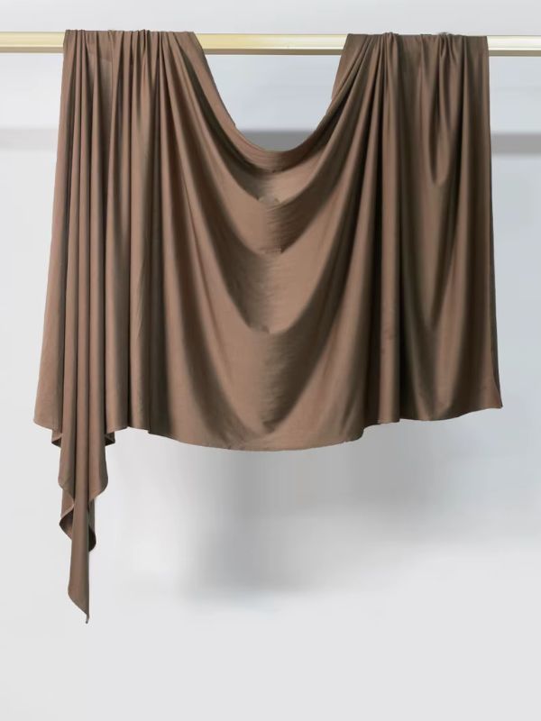 Hijab en jersey marron chocolat suspendu et drapé sur une tringle dorée, présenté sur fond blanc