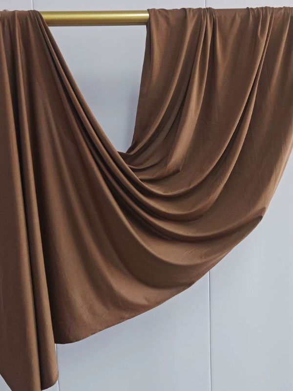 Hijab en jersey cognac suspendu et drapé sur une tringle dorée, présenté sur fond blanc