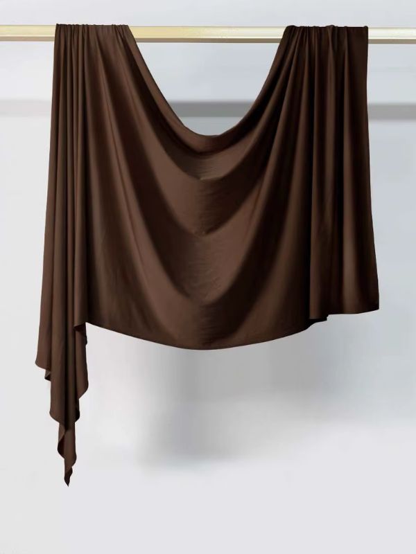 Hijab en jersey marron très foncé expresso suspendu et drapé sur une tringle dorée, présenté sur fond blanc