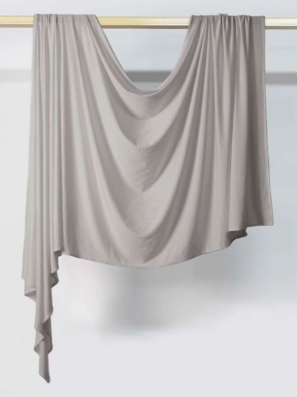 Hijab en jersey gris clair suspendu et drapé sur une tringle dorée, présenté sur fond blanc