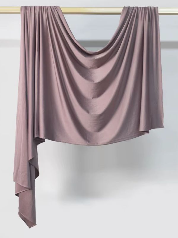 Hijab en jersey mauve poudré suspendu et drapé sur une tringle dorée, présenté sur fond blanc