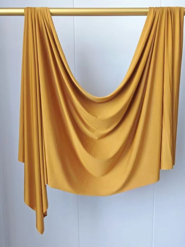 Hijab en jersey jaune moutarde suspendu et drapé sur une tringle dorée, présenté sur fond blanc