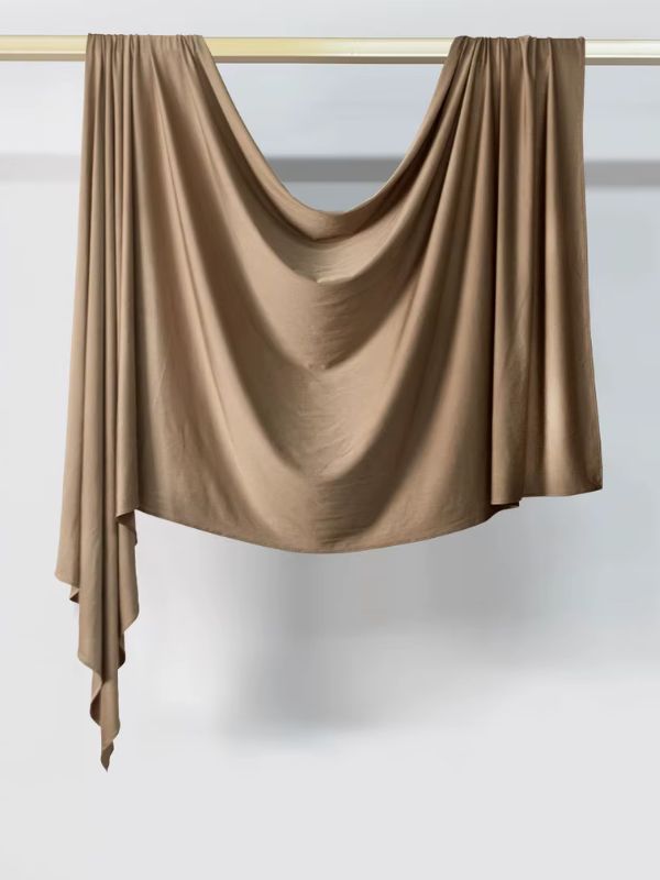Hijab en jersey beige brun noisette suspendu et drapé sur une tringle dorée, présenté sur fond blanc