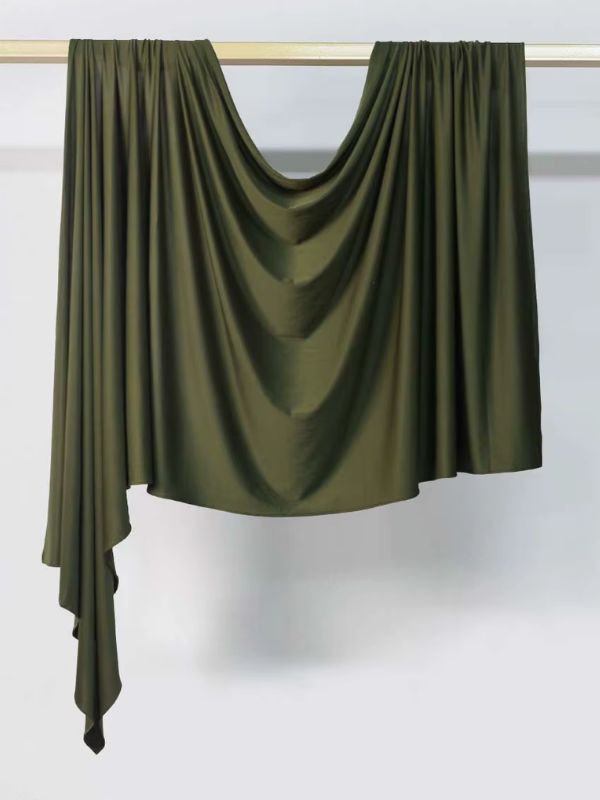 Hijab en jersey vert olive foncé suspendu et drapé sur une tringle dorée, présenté sur fond blanc