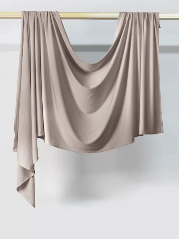 Hijab en jersey taupe suspendu et drapé sur une tringle dorée, présenté sur fond blanc
