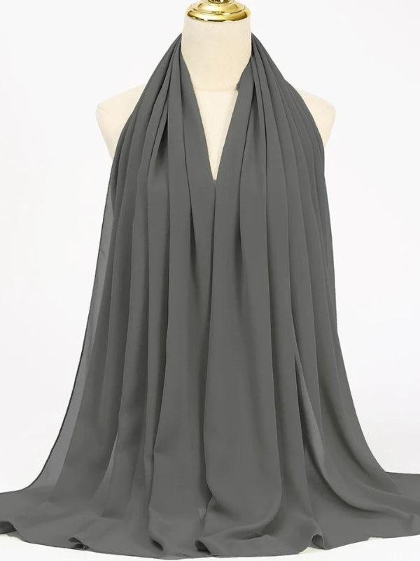 Ce hijab gris est soigneusement drapé sur un mannequin, mettant en valeur son tissu fluide et doux. La couleur grise, sobre et élégante, en fait un accessoire polyvalent qui peut se marier facilement avec diverses tenues. Le tissu semble léger et respirant, offrant à la fois confort et une couverture complète. C'est un choix idéal pour un look à la fois moderne et intemporel