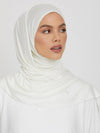 Une femme portant un hijab en jersey blanc, simple et élégant, couvrant entièrement ses cheveux et son cou. Le hijab est drapé avec soin, laissant apparaître son visage serein et son maquillage subtil. Le tissu lisse et soyeux du hijab encadre son visage avec douceur, créant une silhouette fluide et raffinée