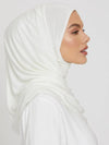 Une femme de profil porte un hijab en jersey blanc, couvrant soigneusement ses cheveux et son cou. Le tissu est lisse et bien ajusté, mettant en valeur ses traits délicats et son maquillage subtil. Son expression est douce et sereine