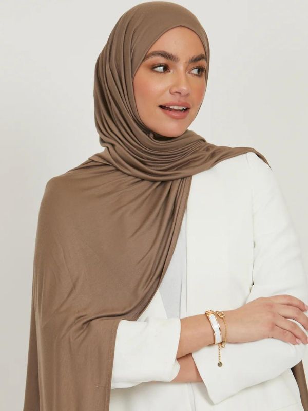Modèle habillée d&#39;un hijab en jersey premium couleur café au lait, posant avec élégance dans une tenue blanche