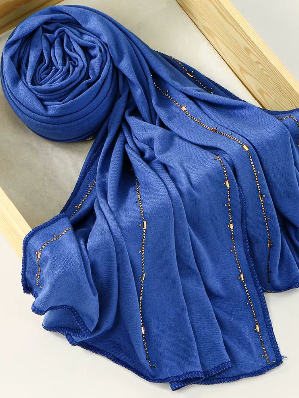 Hijab jersey premium strassé bleu cobalt, enroulé et drapé dans un cadre en bois, lignes de strass dorés sur toute la longueur