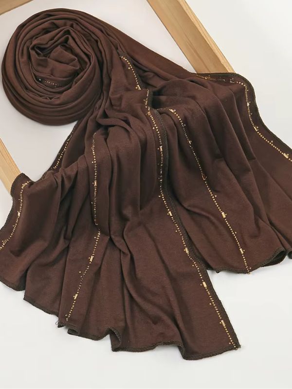 Hijab jersey premium strassé chocolat, enroulé et drapé dans un cadre en bois, lignes de strass dorés sur toute la longueur